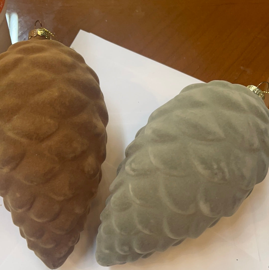 This product includes two Flocked Glass Pinecone ornaments, measuring at 6 1/2" H each. The set provides one in a beautiful taupe color and the other in a sleek gray hue.