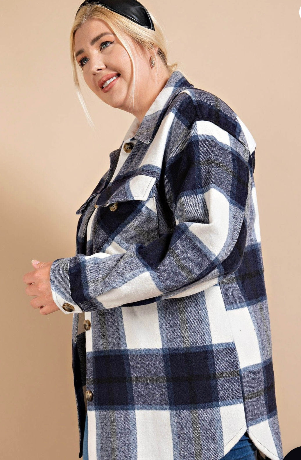 A woman with blonde hair wearing a black headband and a Brushed Plaid Button Down Shirt - PLUS in shades of navy mix and white stands against a beige background, smiling slightly to her right.