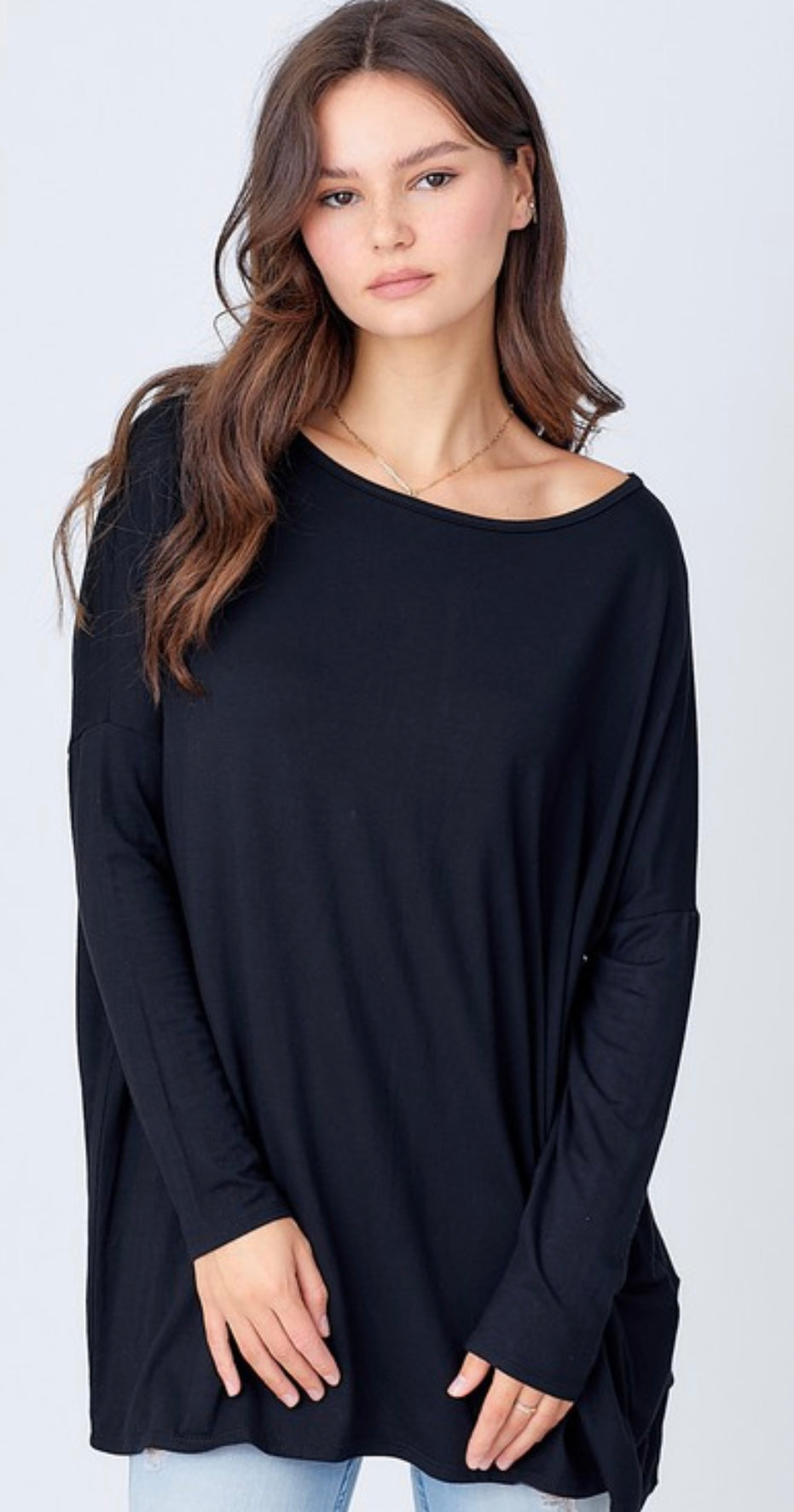 A young woman with long brown hair, wearing a dark blue long-sleeved A.gain “The Perfect Shirt” Long Sleeve Plus and jeans, stands against a white background, looking directly at the camera.