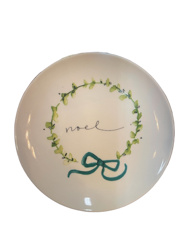 5” round white stoneware plate with "noel" in the center, green wreath design, and blue bow at the bottom.
